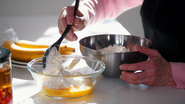 Making pancakes. An old woman adding flour in the dough.
