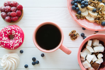 Different kinds of snack and desserts: assortment of fruit pieces, tasty raspberry tart and pink doughnut on white wooden table. A cup of coffee. 