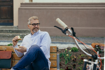 lunch to go. man eating sandwiches in city, bicycle in blurred background