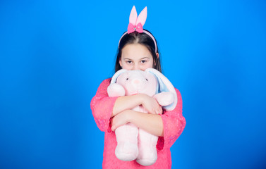 Get in easter spirit. Happy childhood. Bunny ears accessory. Lovely playful bunny child hugs soft toy. Have blessed Easter. Bunny girl with cute toy on blue background. Child smiling play bunny toy