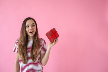 Surprised girl holds in her hand a box with a gift on a pink background.