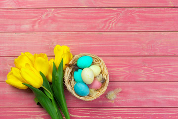 easter, holidays, tradition and object concept - close up of colored eggs and tulip flowers over wooden boards background