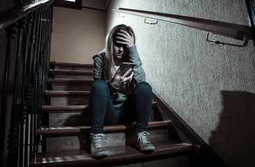 Sad depressed unhappy teenager girl suffering from cyberbullying by mobile smart phone sitting...