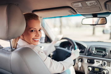 Beautiful businesswoman driving a car, smiling at camera.