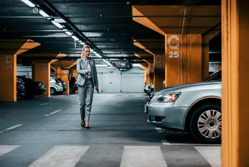 Fototapeten Successful businesswoman walking to her car in underground car parking. © bnenin