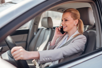 Smiling female executive talking on mobile phone and driving.