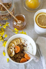 Breakfast of granola with yogurt and tea and forsythia flowers on a linen tablecloth. Rustic style.