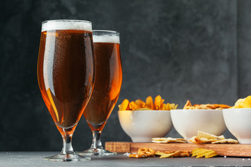 Glass of lager beer with snack bowls on dark stone background