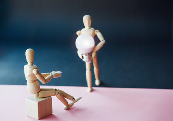 Two wooden little man, the first is sitting in anticipation of help, the second is going to meet with positive new ideas. Сoncept of support and mutual assistance between people.