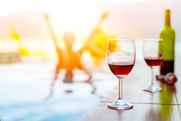 Two glasses of red wine near the swimming pool with a man is swimming in the pool