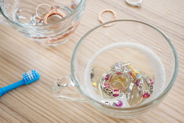 cleaning jewelry diamond ring with glass of hot water and dishwashing liquid on wood table background