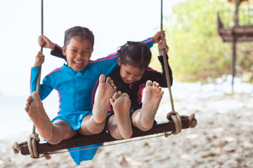 Children bare feet with sand while they playing on a swings together at the beach near the sea in summer vacation