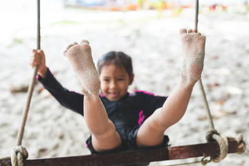 Child feet with sand while she playing on a swing at the beach near the sea in summer vacation