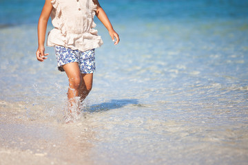 Leg of little child girl running on beach with water splashing in summer vacation