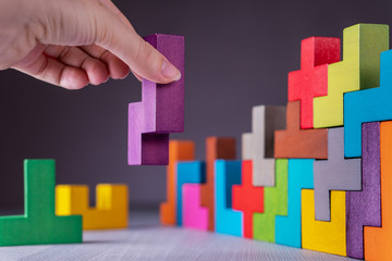 Geometric shapes on a wooden background. Hand sets the element of the puzzle.