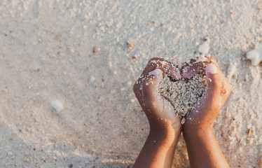 Child girl holding sand make heart shape in hands and playing on the beach in summer vacation