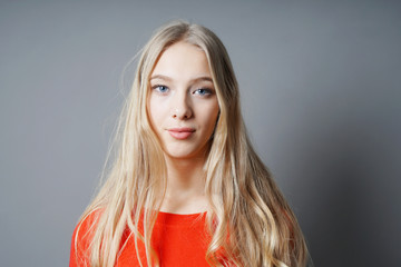 young teenage woman with long blond hair, pale skin and blue eyes against gray background with copy...