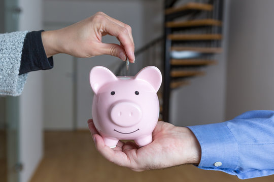 Frau steckt eine Münze in den Sparschwein, den ein Mann in seiner Hand festhält, sie sparen für eine Eigentumswohnung