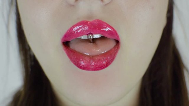 Sexy female lips of bright color. The girl licks her lips. She has a tongue piercing.