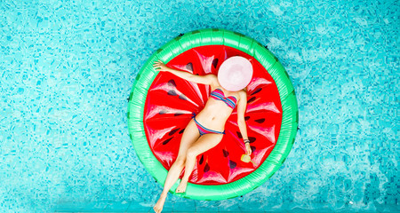 Young woman relaxing on watermelon lilo in villa resort pool - obrazy, fototapety, plakaty