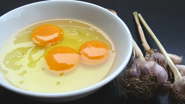 Fresh chicken eggs fall in a white mixing bowl and have fresh garlic on the side. Prepare for making an omelette.