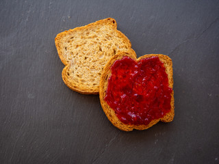 Two slices of toast with raspberry jam on a slate plate