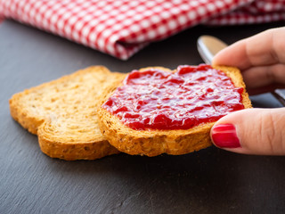 A woman with nails painted red with a slice of toast in her hand with raspberry jam