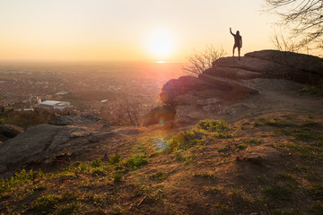 Man in black track suit standing on mountain cliff in sunset. People in nature.