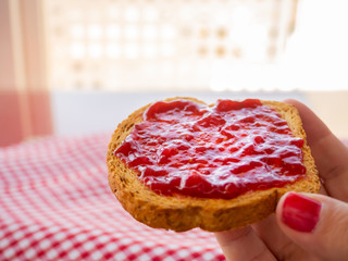 A woman with nails painted red with a slice of toast in her hand with raspberry jam