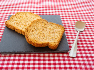 Two slices of toast on a slate plate, one old spoon and tablecloth vintage style
