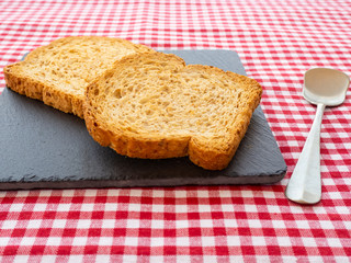 Two slices of toast on a slate plate, one old spoon and tablecloth vintage style