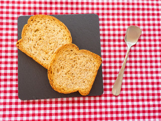 Two slices of toast on a slate plate, one old spoon and tablecloth vintage style