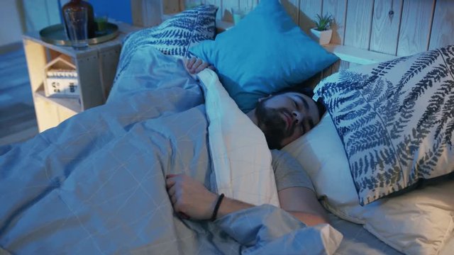 Scared young man opening eyes. Bearded guy waking up to crying of baby behind wall at two o'clock in morning. Indoors. Home. Flat. Night time.