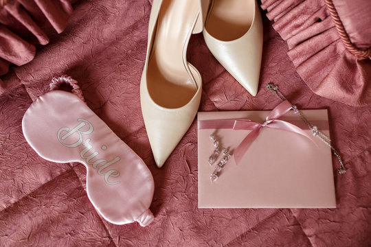Wedding. Accessories for bride: уngagement ring and two wedding rings near bridal shoes on on high heels, perfume bottle, wedding invitation, earrings and sleep eye mask with inscription "Bride"
