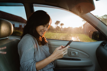young asian woman using mobile phone while on passenger seat in the car