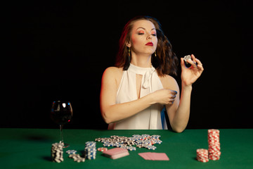 Emotional young lady in a white blouse drinking wine from a glass and playing cards on a table on...