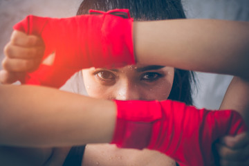 Image focus the eyes of the beautiful young Asian boxers. She is a martial arts athlete, strong face filled with sweat, her eyes are committed. Two of her hands with red boxing bandage hand wrap.