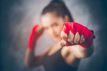 Image focus the fist of the beautiful young Asian boxers. She is a martial arts athlete, strong face filled with sweat, Two of her hands with red boxing bandage hand wrap. Woman power with copy space. - Powered by Adobe