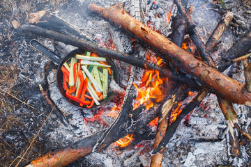 Cooking dishes from red bell peppers and cucumbers in a pan on a fire