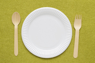 Wooden single use kitchenware on green napkin. Top view, space for text.