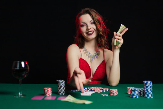 Emotional young lady in an evening red dress playing cards on a table on green cloth in a casino