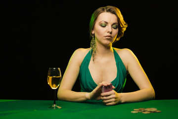 A young lady in a green dress is playing solitaire made from scrying cards on a table on a green...