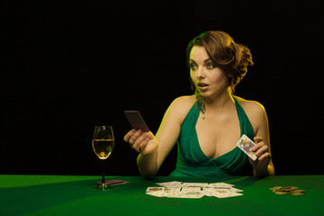 A young lady in a green dress is playing solitaire made from scrying cards on a table on a green...