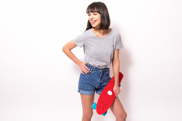 Full length portrait of a pretty young woman in sunglasses posing with skateboard while standing and looking at camera isolated over white background
