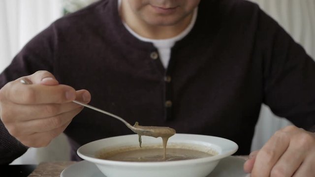 The man at the cafe table is slowly eating soup. Business lunch
