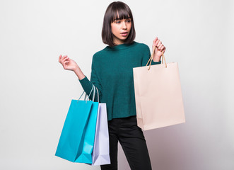 Fototapeta premium Portrait of a smiling woman dressed in green sweater holding shopping bags and looking away isolated over white background