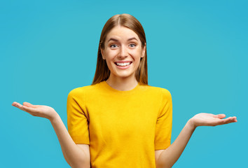 Smiling young girl looks at camera and spreads hands. Photo of attractive girl shows open palms...