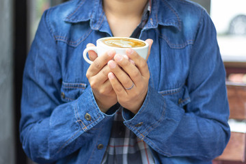 woman wearing blue jean shirt and hand holding a cup of flat white coffee