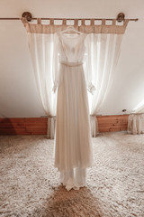 stylish and beautiful wedding dress. classic lace silk wedding dress hanging on hanger in hotel wooden room. morning preparation wedding concept.