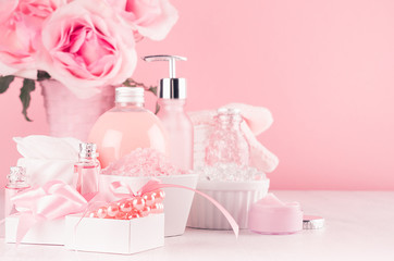 Romantic bathroom interior in pastel pink and silver color - flowers, bath accessories, pearls, gift, cosmetic products - cream, salt, rose oil, soap on white wood table.